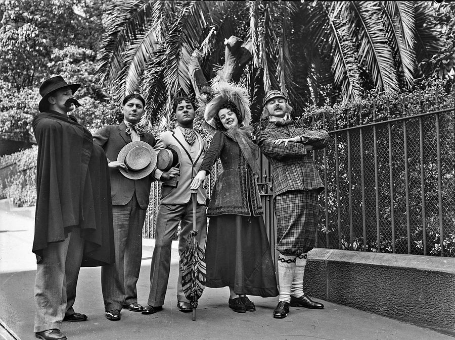 Five performers in theatrical costume beside a wire fence — photograph, 1850–1949