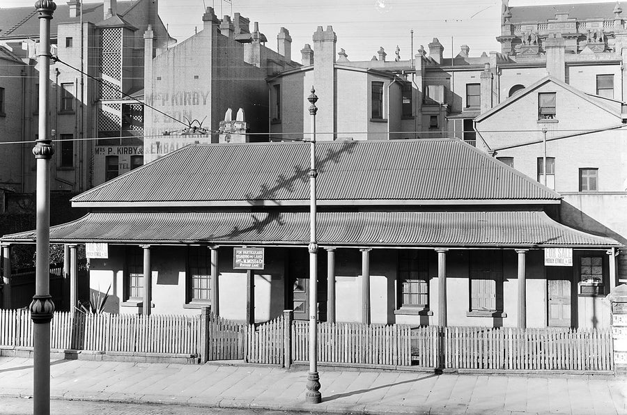 Cottage marked for sale beneath ironmongers' wall signs, Sydney — photograph, from Sydney, c. 1890–1905