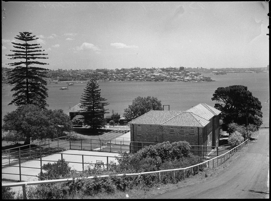 Harbour view past a tennis court and brick house — photograph, from null, circa 1950