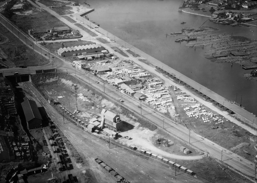 Hume Pipe Co. yard and timber booms along an industrial waterfront, Rozelle — photograph, from Rozelle Bay, circa 1930