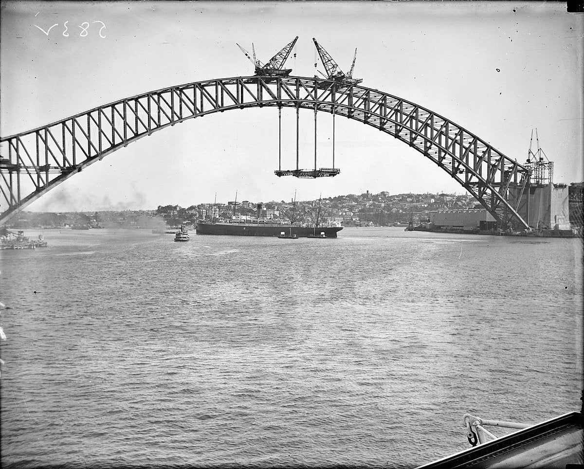 Hoisting a deck section beneath the completed arch, Sydney Harbour Bridge, circa 1930 — photograph, from Northcliff Street, circa 1930