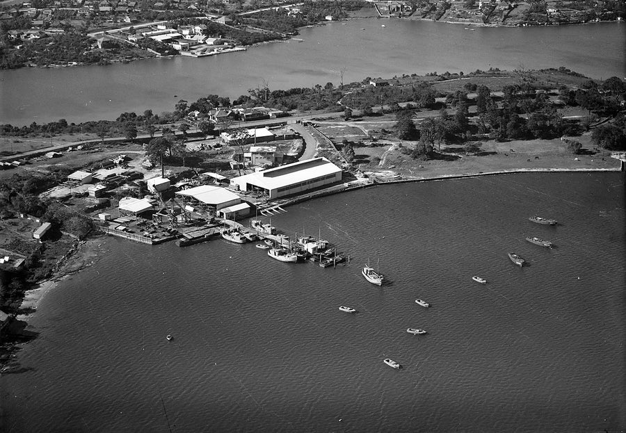 Aerial view of a riverside boatbuilding works with moored craft — photograph, from Homebush West, 1930–50