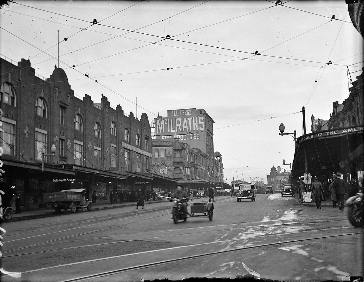 Darlinghurst streetscape with trams, traffic and the McIlrath's grocery sign, 1934 — photograph, from Darlinghurst, circa 1934