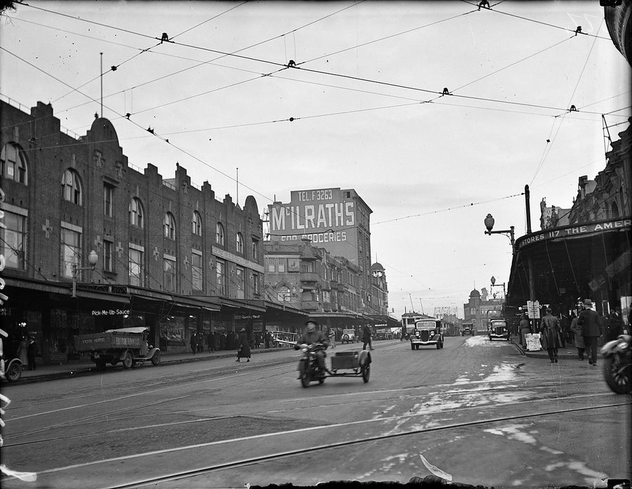 Darlinghurst streetscape with trams, traffic and the McIlrath's grocery sign, 1934 — photograph, from Darlinghurst, circa 1934