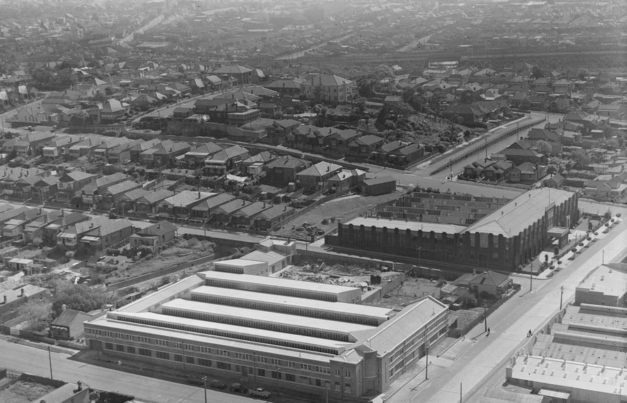 Aerial view of a sawtooth-roofed factory among suburban housing — photograph, circa 1940