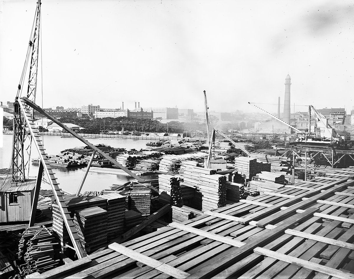 Stacked timber and cranes at Hudson's Timber Yard, Blackwattle Bay — photograph, from Sydney Secondary College Blackwattle Bay Campus, c. 1920–25