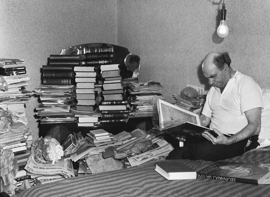 Book collector reading amid stacks of volumes, Marrickville — photograph, from Marrickville, circa 1949
